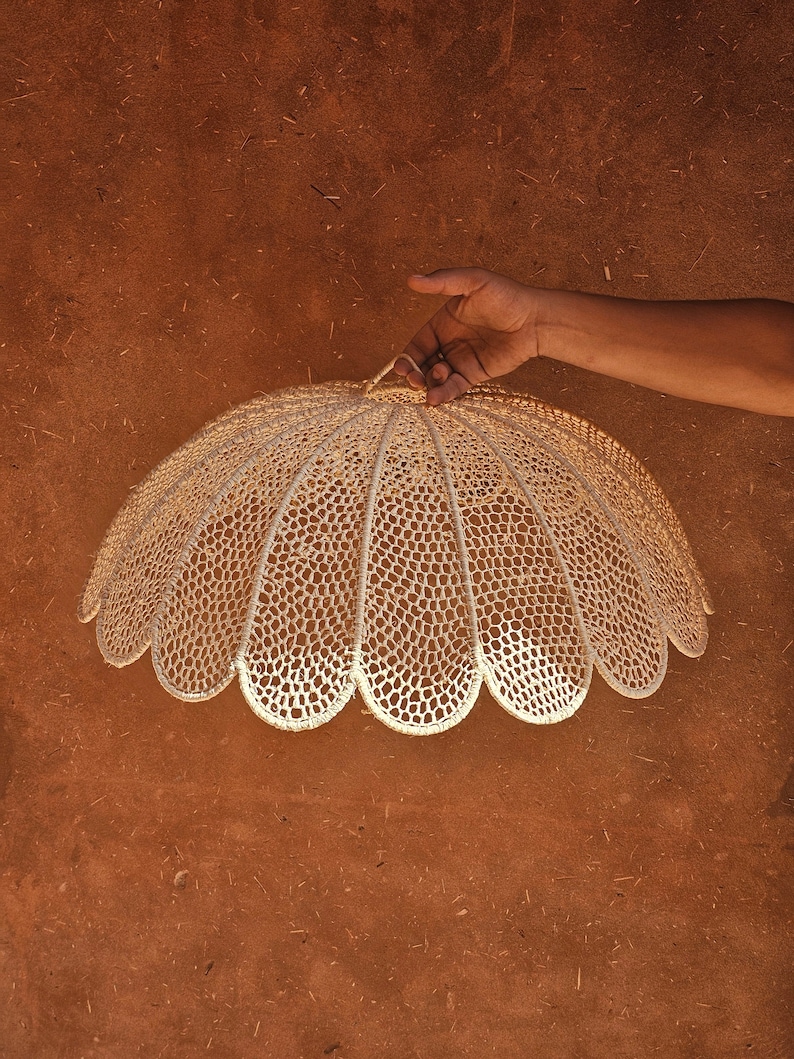 May include: A white crocheted lampshade with a scalloped edge, hanging from a hand.