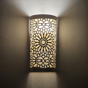 May include: A white wall sconce with a geometric pattern and a light bulb illuminating the intricate design.