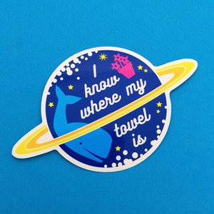 May include: A blue and white sticker with a whale and a ring around it. The sticker says "I know where my towel is".