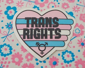 May include: A heart-shaped sticker with the text "TRANS RIGHTS" in black letters on a pink, white, and blue background. The sticker also features a transgender symbol.