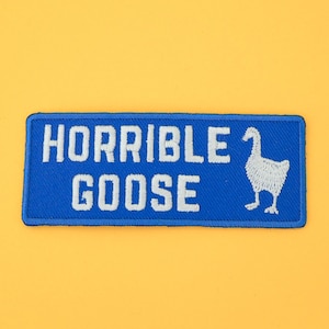 Peut inclure: Écusson brodé bleu avec du texte blanc qui dit "HORRIBLE GOOSE" et une illustration de  oie blanche.