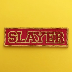 May include: Red embroidered patch with gold stitching that says "SLAYER" in all caps.
