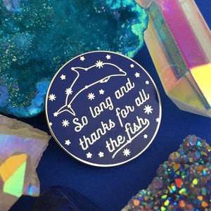 May include: A blue enamel pin with a white dolphin and stars, and the text "So long and thanks for all the fish".