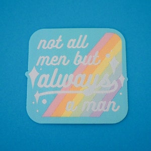 Puede incluir: Un parche azul claro con un diseño de arcoíris y el texto "not all men but always a man" en blanco.