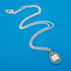 Silver-plated curb chain necklace with an enamel charm pendant. Charm is a teal, egg-shaped virtual pet toy. On the screen is a silver stegosaur & game icons. Beneath the screen are 3 buttons and above are a heart and shooting star in bright colours.