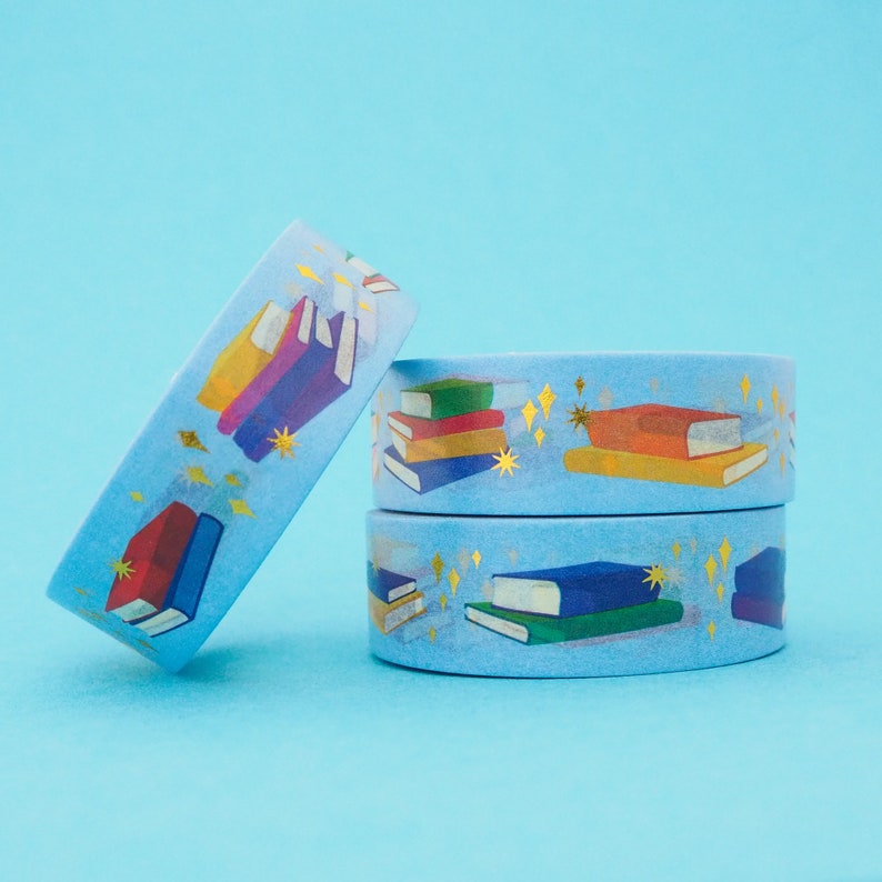 Light blue washi tape printed with small stacks of colourful books and gold-foil sparkles.
