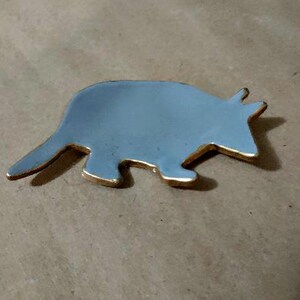 May include: A silver-colored metal animal figurine shaped like an armadillo. The figurine has a smooth, shiny surface and is outlined in gold.