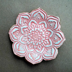 May include: A pink and white ceramic dish with a gold rim, featuring a detailed mandala design. The dish is shaped like a flower with multiple petals.