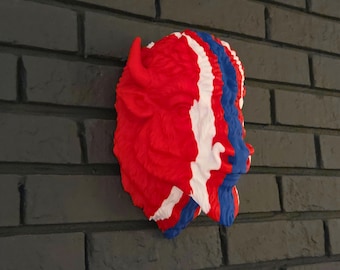 Op de afbeelding: Een wandsculptuur van een bizonkop met een verticaal kleurpatroon in helderrood, wit en blauw. Het getextureerde oppervlak toont de vacht en de gelaatstrekken van het dier, inclusief een zichtbare hoorn en een snuit.