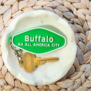 May include: A green and white motel key chain with the text "Buffalo An All America City". The key chain is sitting on a white marble dish.