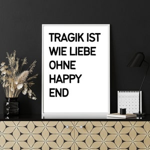 May include: A white framed print with black text that reads "Tragik ist wie Liebe ohne Happy End". The print is on a black surface with a gold patterned cabinet below.