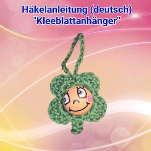 May include: A handmade green crochet cloverleaf ornament with a smiling face and blue eyes. The ornament has a wooden center and a loop for hanging. The text "Häkelanleitung (deutsch) "Kleeblattanhänger"" is at the top.