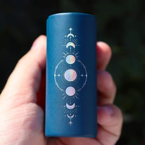 Peut inclure: Un r&eacute;cipient cylindrique bleu fonc&eacute; avec un motif de lune et d'&eacute;toile blanc. Le motif pr&eacute;sente cinq lunes dans diff&eacute;rentes phases, entour&eacute;es d'&eacute;toiles et d'un cercle.