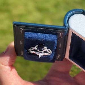 Peut inclure: Une bague de fian&ccedil;ailles ovale noire avec un halo de diamants et une alliance assortie. La bague est dans un &eacute;crin &agrave; bague en velours bleu.