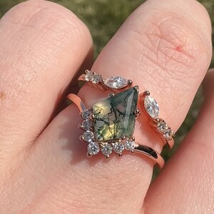 Könnte beinhalten: Ein Ring aus Roségold, besetzt mit einem grünen Moosachat-Edelstein und einem Heiligenschein aus klaren Zirkonia-Steinen. Der Ring wird an einem Finger mit einem passenden Roségoldband mit klaren Zirkonia-Steinen getragen.