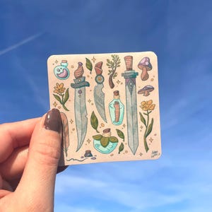 Puede incluir: Una pegatina cuadrada con ilustraciones de dagas, botellas de pociones, setas y elementos florales. La obra de arte tiene una paleta de colores suaves con un fondo marrón claro y un cielo azul de fondo.