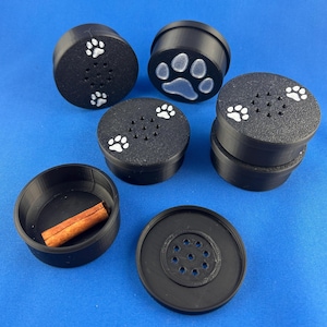 Peut inclure: Six contenants en plastique noir avec des motifs de pattes de chien et un septième contenant avec un bâton de cannelle à l'intérieur. Les contenants ont de petits trous sur le dessus.
