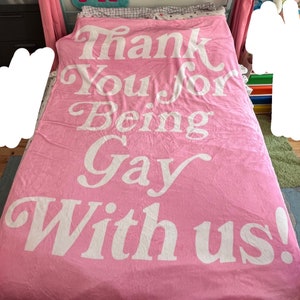 Könnte beinhalten: Rosafarbene Kuscheldecke mit dem Text "Thank You for Being Gay With Us!" in weißen Buchstaben.