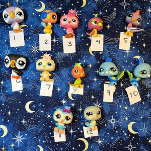 May include: Twelve colorful plastic bird figurines with different designs and colors. The birds are arranged in two rows on a blue background with white stars.