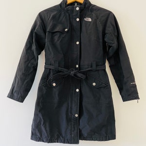 May include: Black long-sleeved jacket with a belt, snap buttons, and a zipper. The jacket has a logo that says "The North Face" on the left side of the chest. The jacket has a label that says "HyVent" on the right side of the jacket.