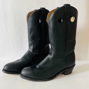 Op de afbeelding: Een paar zwarte leren cowboylaarzen met een spitse neus en een blokhak. De laarzen hebben een decoratief stikseldetail rond de bovenkant van de schacht en een klein gaatje aan elke kant van de schacht.