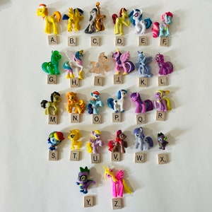 May include: A collection of 26 colourful My Little Pony figurines, each with a unique design and pose. The figurines are arranged in alphabetical order from A to Z, with each letter labelled on a small square below the figurine.
