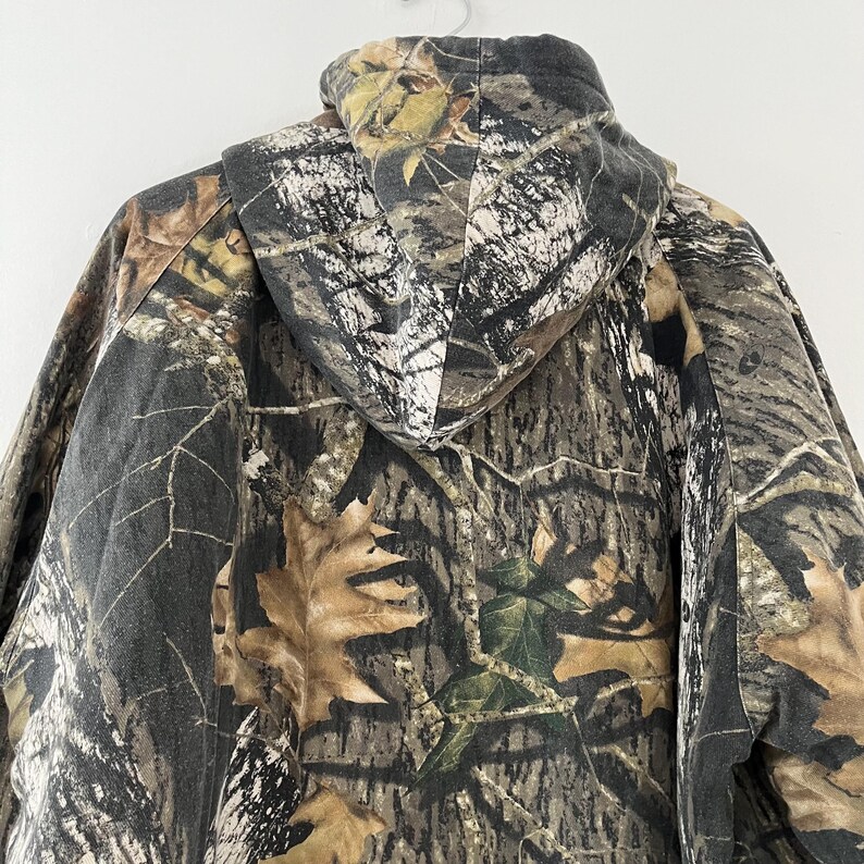 May include: Camouflage hooded sweatshirt with a brown, green, and white pattern. The hoodie is made of a soft, comfortable fabric and has a drawstring.