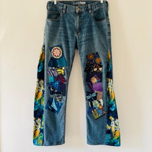 Könnte beinhalten: Blaue Jeans aus Denim mit bunten Stoff-Patches, die auf die Beine genäht sind. Die Patches zeigen verschiedene Designs, darunter Blumen, Sterne und geometrische Muster.