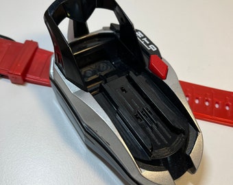 Może przedstawiać: Czarno-srebrna zabawka z czerwonym przyciskiem z napisem "HOLD". Zabawka ma czarną plastikową podstawę ze srebrną obwódką i czarny plastikowy uchwyt.