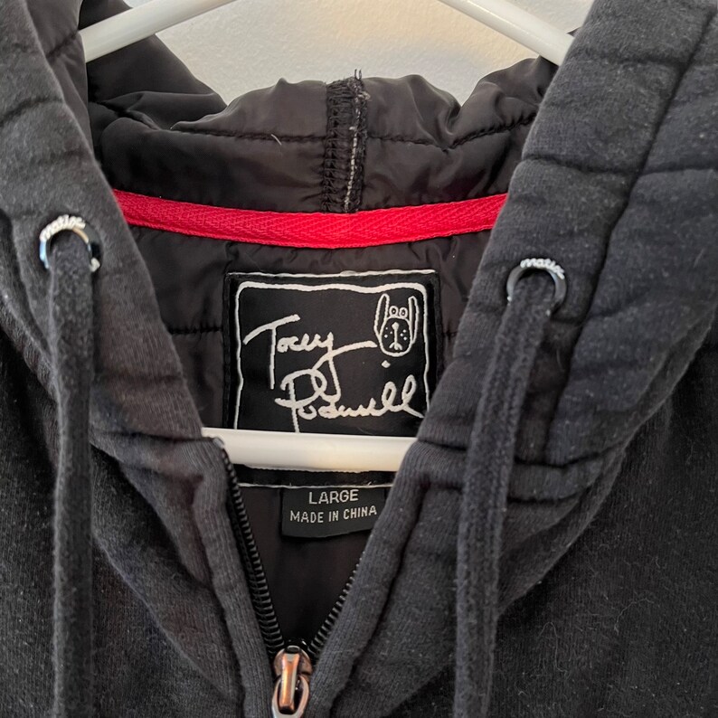 May include: Black hooded sweatshirt with a red zipper and a white label that says "Tony Posenell" with a cartoon dog logo. The label also says "Large" and "Made in China".