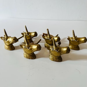 May include: A set of six gold-colored metal cabinet knobs, each shaped like a unicorn head with a spiraled horn. The knobs feature a textured finish and include a metal screw extending from the back of each unicorn head for mounting purposes.