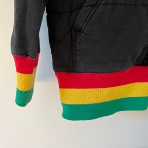 May include: Black hoodie with red, yellow, and green trim around the cuffs and bottom hem.