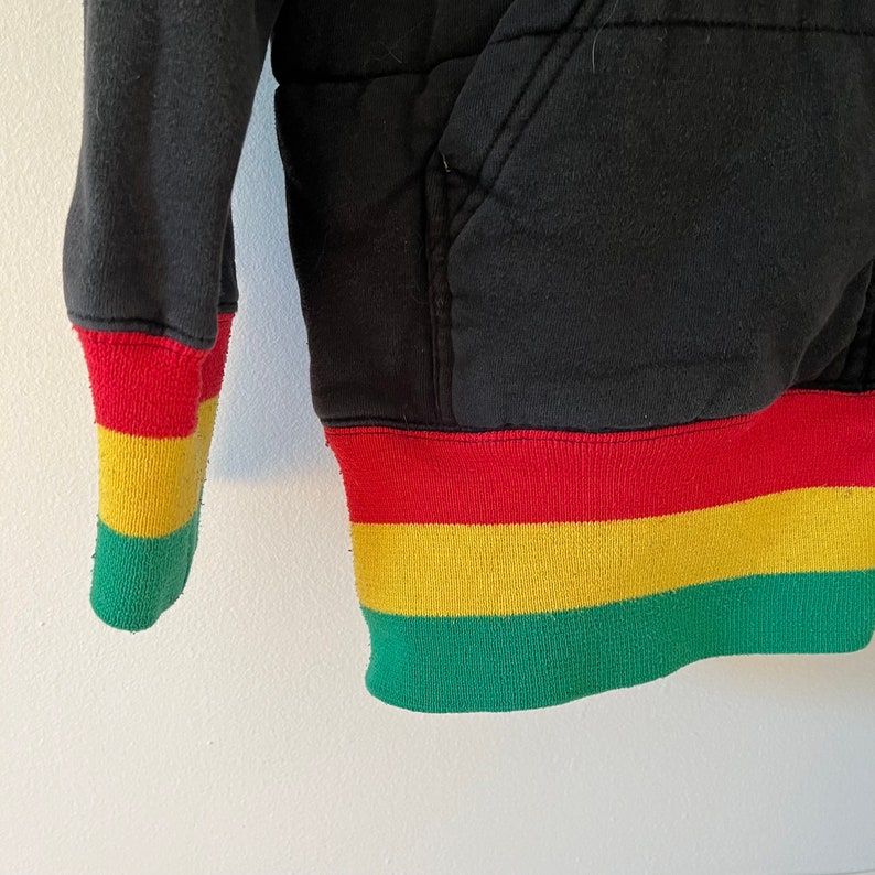 May include: Black hoodie with red, yellow, and green trim around the cuffs and bottom hem.