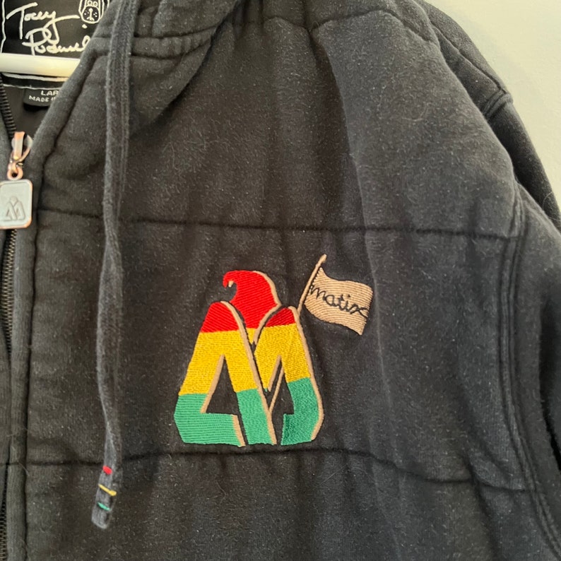 May include: Black quilted zip-up hoodie with a large embroidered logo featuring a mountain with a flag that says "Matix".