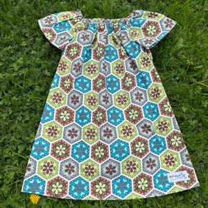 Könnte beinhalten: Ein kurzärmeliges Kleid mit einem geometrischen Blumenmuster in Grün-, Braun- und Blautönen. Das Kleid hat einen Off-Shoulder-Ausschnitt und ein gerafftes Oberteil. Der Stoff ist leicht und scheint Baumwolle zu sein.