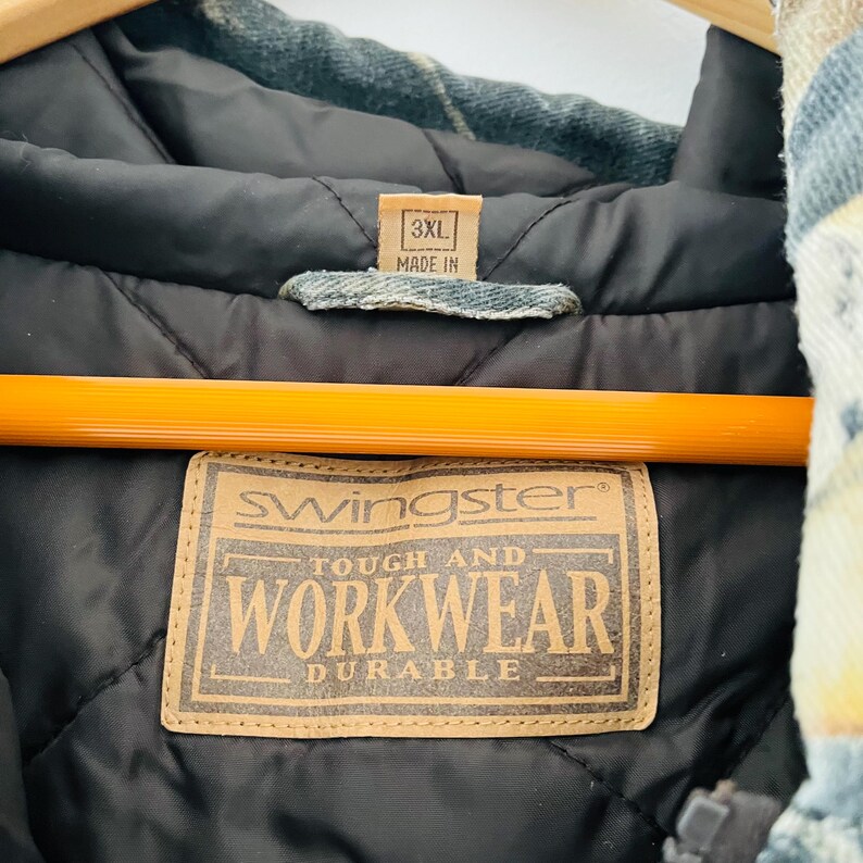 May include: A brown leather patch with the text "Swingster Tough and Workwear Durable" on a blue and green plaid jacket with a 3XL size tag that says "Made in".