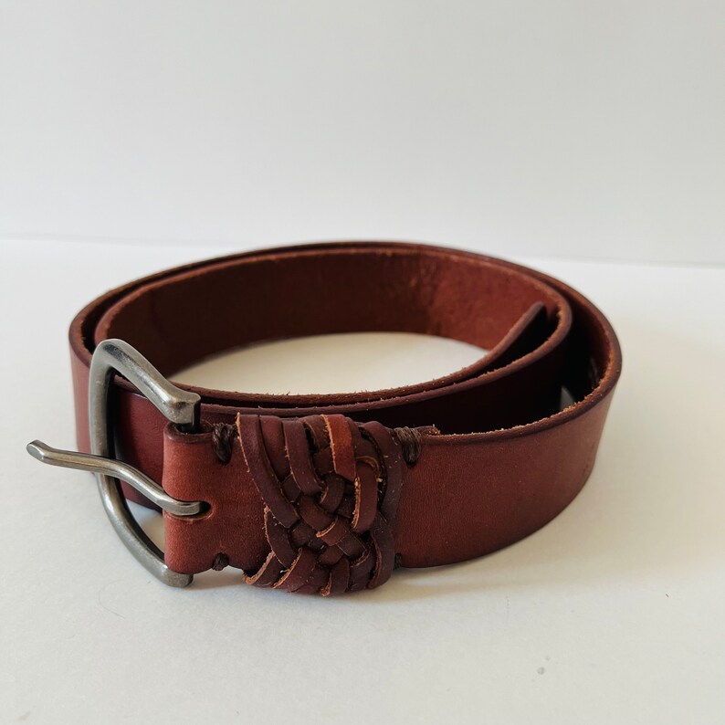 May include: A brown leather belt with a braided design and a silver buckle.