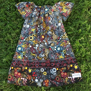 Puede incluir: Un vestido blanco y negro con un patrón colorido de círculos y remolinos. El vestido tiene mangas cortas y un escote fruncido. La tela tiene un aspecto y una textura texturizados. El vestido tiene una etiqueta que dice "sewfunky.ca".