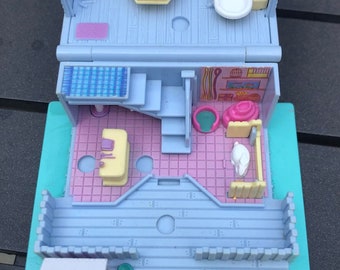 May include: A blue and pink plastic dollhouse with a white bathtub, a yellow tub, and a blue and white tiled roof. The dollhouse has a green and blue lawn and a pink brick walkway. The dollhouse is made by the toy company, "PlaySkool".
