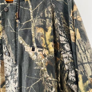 May include: A camouflage jacket with a hood and a black "BUCK" logo with the words "MOUNTAIN DEERE" above it.