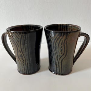 May include: Two ceramic mugs with black and green glaze. The mugs have a wood grain pattern and a flared shape.