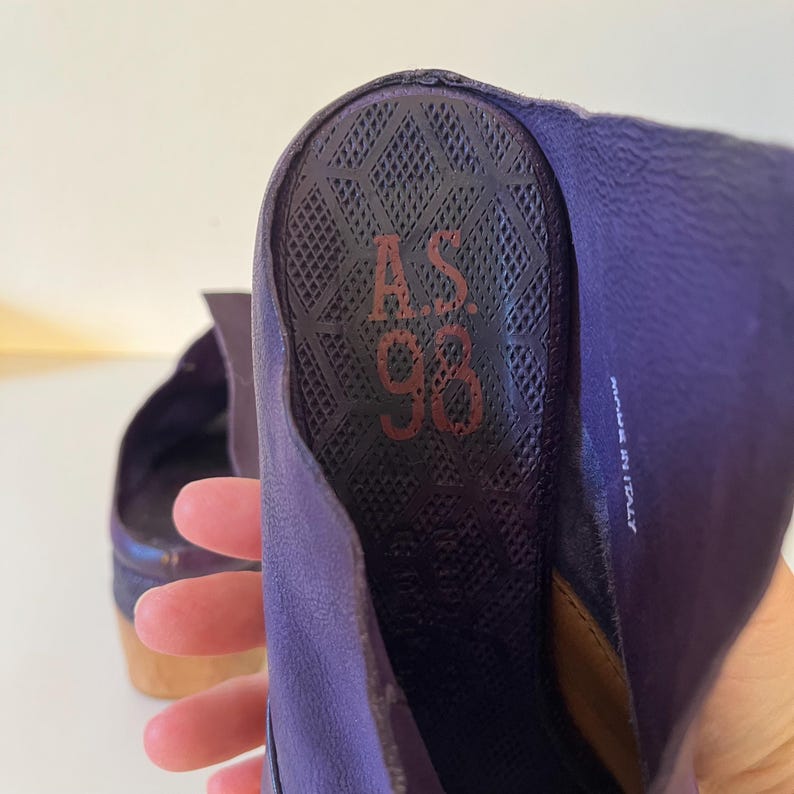 May include: Close-up of a purple shoe interior with the text "A.S. 98" in red. The shoe's insole has a textured pattern. The words "MADE IN ITALY" are visible on the side. The shoe has a wooden heel.