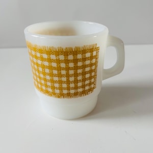 Op de afbeelding: Witte keramische mok met een geel ruitpatroon aan de zijkant. De mok heeft een oor en een licht uitlopende bovenkant. Het ontwerp is klassiek en in vintage stijl.
