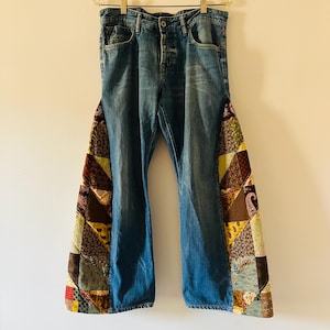 Peut inclure: Un jean bleu en denim à pattes d'éléphant avec des empiècements en tissu patchwork sur les côtés. Le tissu patchwork est composé de différentes couleurs et motifs, dont le brun, le vert, le jaune et le rouge.