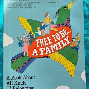 May include: A book cover with a colorful illustration of a bird with wings shaped like hearts. The bird is carrying people of different races and ages. The title of the book is "Free to Be... A Family". The subtitle is "A Book About All Kinds of Belonging".