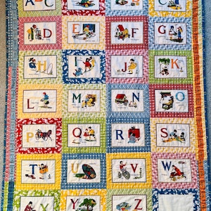 Puede incluir: Una colcha de alfabeto colorida con cada letra del alfabeto representada por una imagen diferente. La colcha está hecha de una variedad de telas y colores, y cada cuadrado está bordeado con un marco blanco. La colcha es perfecta para la habitación de un niño o una guardería.