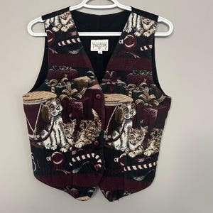 Op de afbeelding: Een tapijtweefsel vest met een zwarte achterkant en een voorkant met een herhalend patroon van honden, katten en cadeau dozen. Het vest heeft een V-hals, twee knopen en een label met de tekst "Southern Traditions".