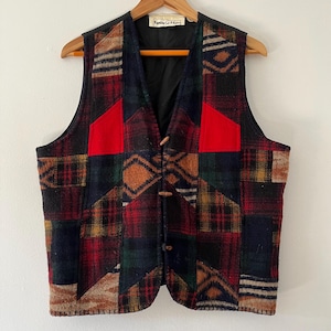 May include: A patchwork waistcoat featuring a mix of plaid and patterned fabrics in red, green, blue, and brown. The waistcoat has a black lining, two red accent patches, and wooden button fastenings. It is displayed on a wooden hanger.