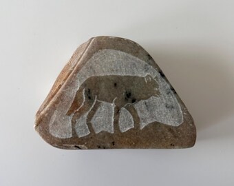 Può includere: Una scultura in pietra scolpita di un lupo, il lupo è scolpito in bianco su uno sfondo di pietra marrone.