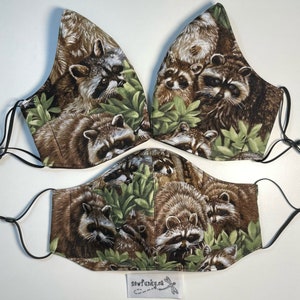 May include: Three brown and green fabric face masks with a raccoon print. The masks feature a variety of raccoons in different poses, surrounded by green leaves. The masks are made of a soft, comfortable fabric and are perfect for everyday use.